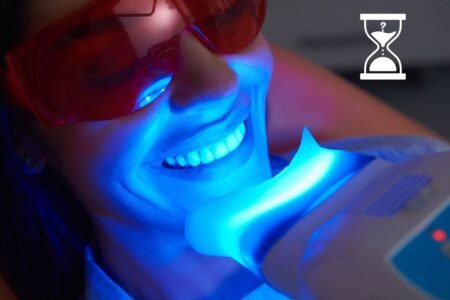 Femme portant des lunettes de protection rouges souriant sous une lumière bleue lors d'un traitement de blanchiment dentaire.